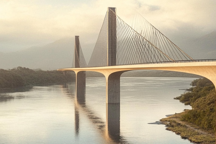 Puente atirantado grande que cruza un río ancho. El puente tiene dos torres principales con cables que se extienden desde ellas para soportar la plataforma del puente. La zona circundante incluye vegetación y agua tranquila que refleja la estructura del puente. El cielo parece estar nublado con nubes, creando una atmósfera serena.